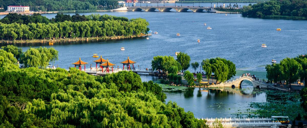 A river with boats, a bridge, a city skyline, and a park with pagodas.