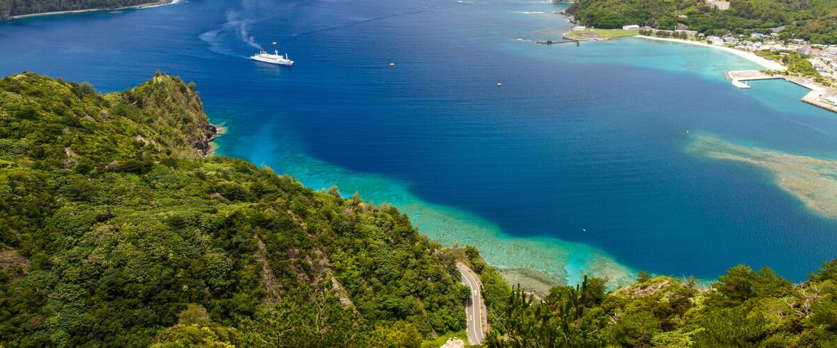 A coastal landscape with a clear blue sea, a white boat, and lush green hills.