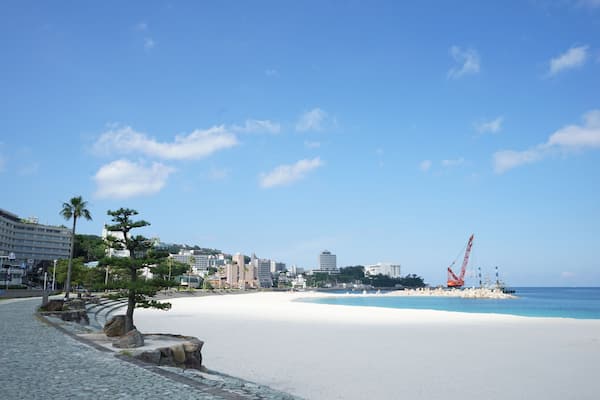 Uma praia com areia branca, céu azul límpido e uma grua de construção ao longe.