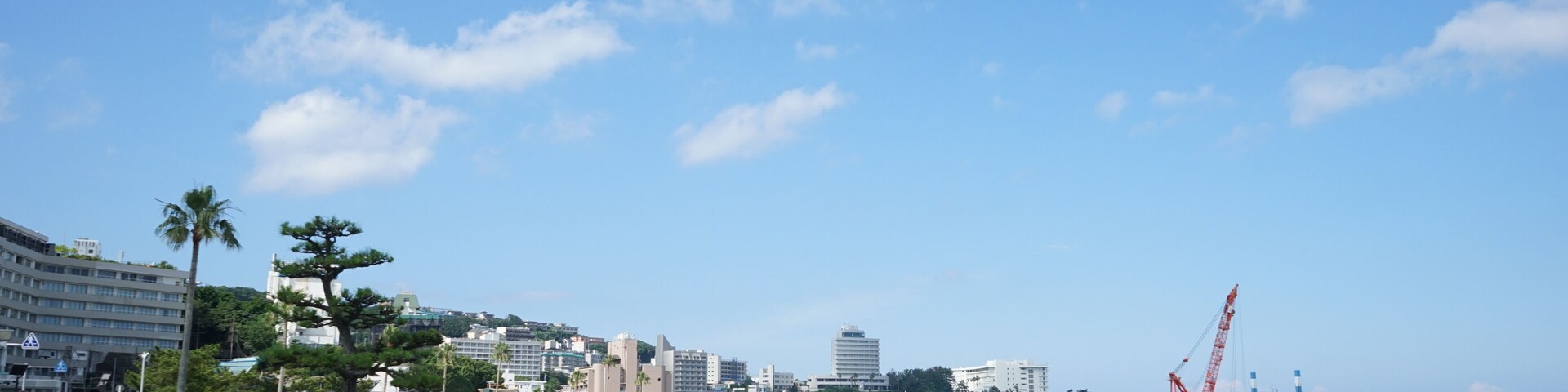 Uma praia com areia branca, céu azul límpido e uma grua de construção ao longe.