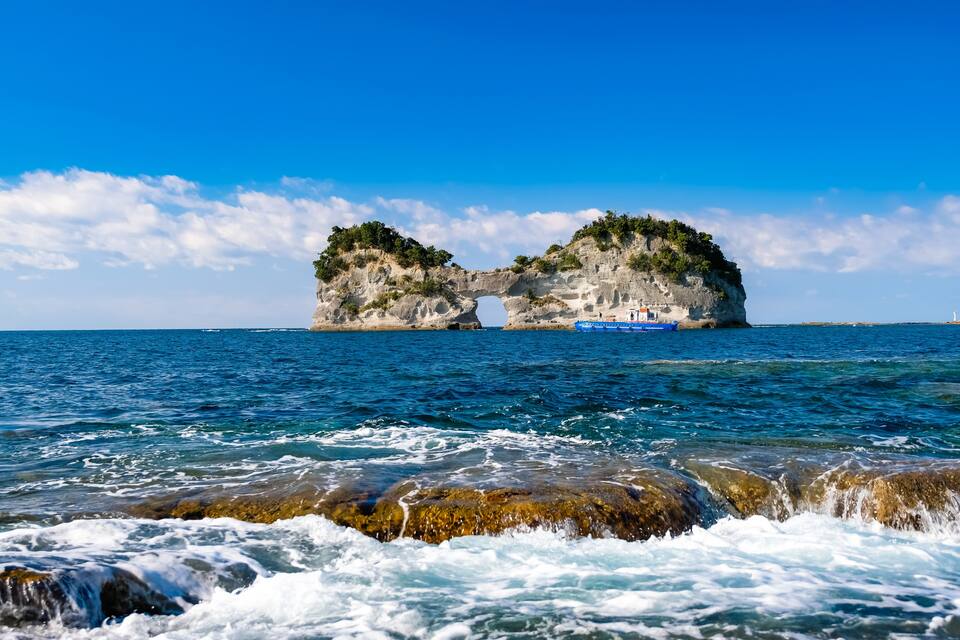 A coastal rock formation with a natural arch and a boat in the water.