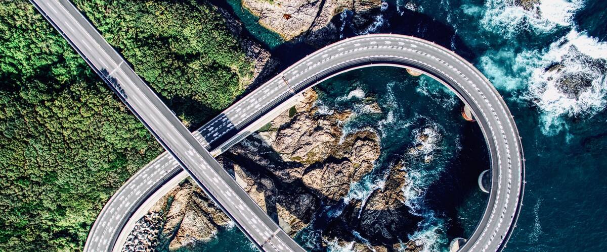 A circular road bridge over a coastal area with rocky terrain and dense greenery.