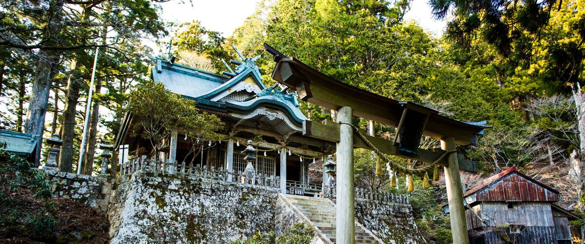 A traditional Japanese temple with a staircase leading up to a shrine, surrounded by trees and stone structures.