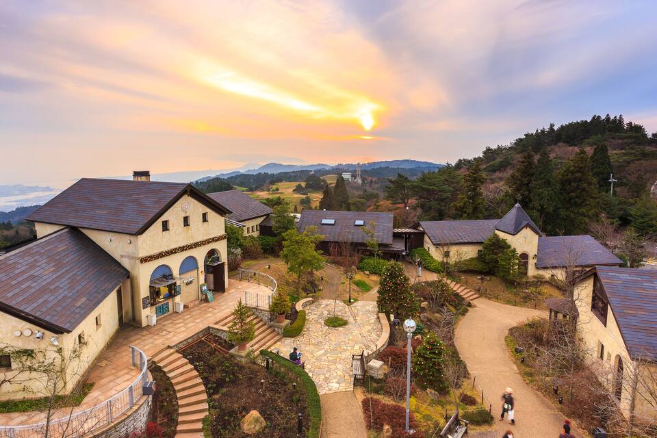 A village with stone pathways, traditional buildings, and a sunset over rolling hills.