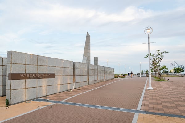 Eine Gedenkstätte mit Inschriften, ein hohes Denkmal und ein gepflasterter Weg mit Straßenlaternen.