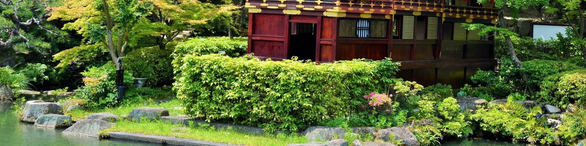 A traditional Japanese building surrounded by lush greenery and a pond.