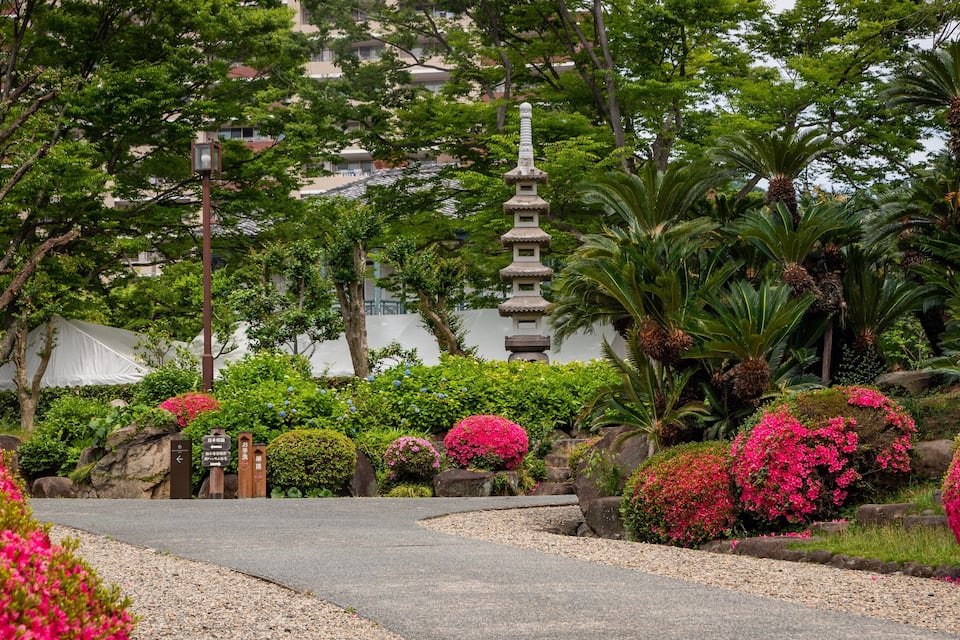 A garden with a stone pagoda, pink flowers, and lush greenery.