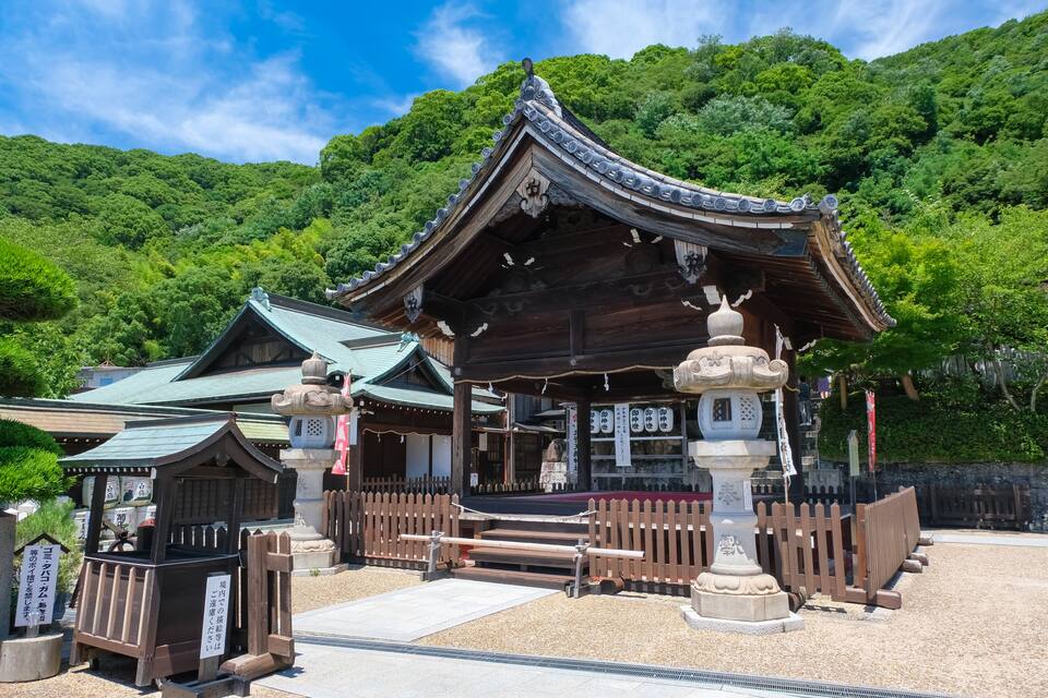 A traditional Japanese temple with a wooden structure, surrounded by lush greenery and hills.