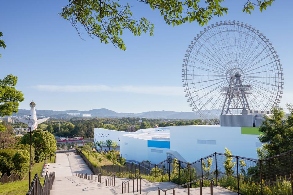 A large Ferris wheel, a white building, and a statue in a park.