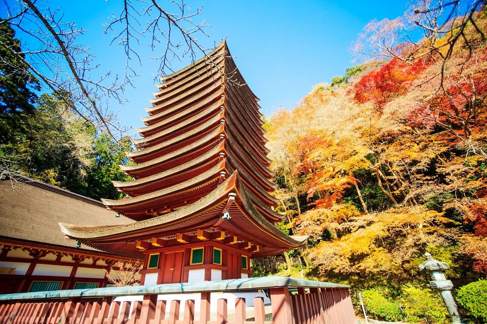 Een traditionele Japanse pagode met een gebogen dak, omringd door bomen met herfstkleuren.
