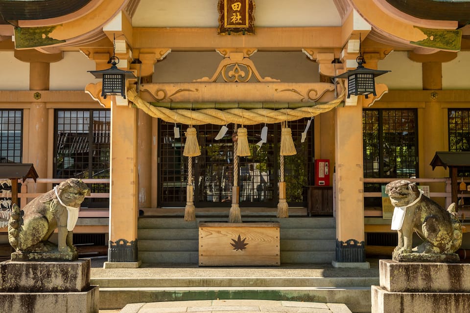 Une entrée de temple japonais traditionnel, ornée de statues de lions en pierre, de portails torii en bois et de lanternes suspendues.