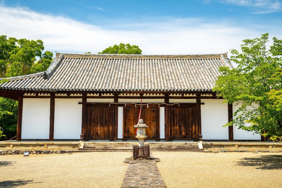 Un bâtiment traditionnel japonais, avec un toit recouvert de tuiles, des portes en bois et une lanterne en pierre dans la cour.