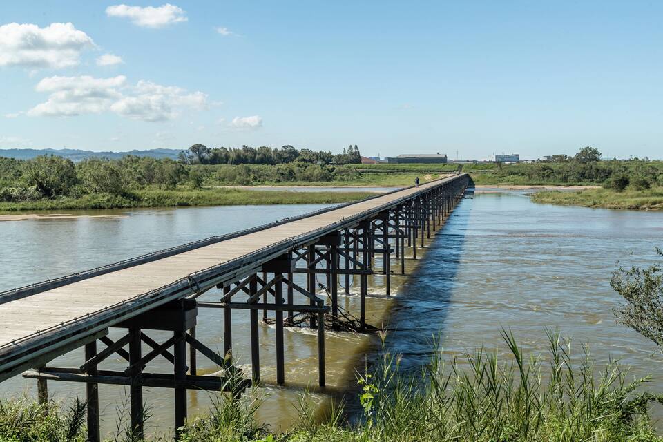 Un lungo ponte di legno che sovrasta un fiume, con cielo sereno.