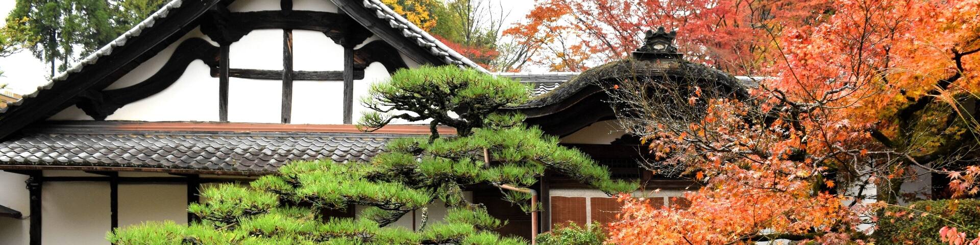A traditional Japanese building with a tiled roof, surrounded by well-maintained gardens and autumn-colored trees.