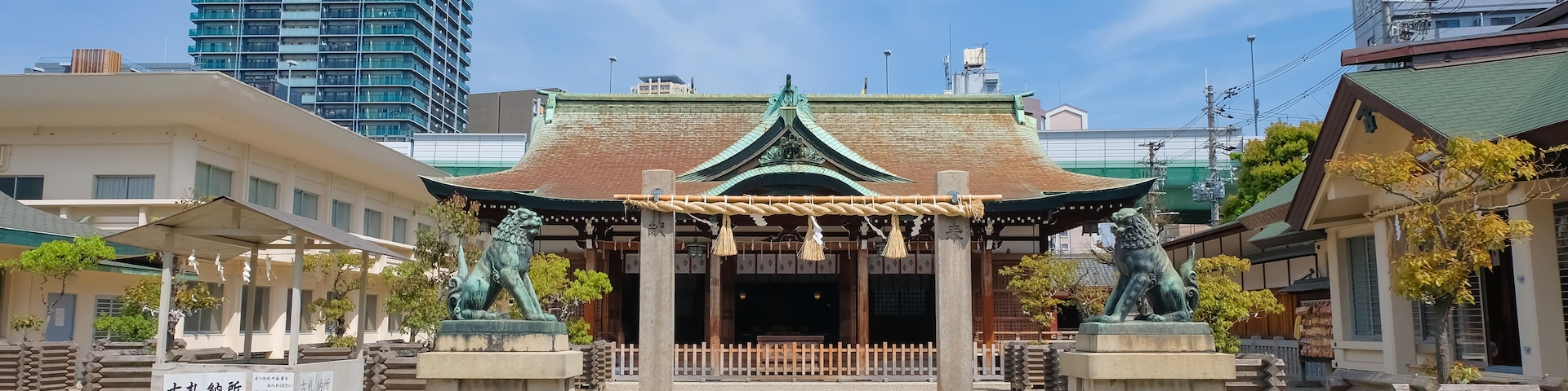 Um templo japonês tradicional com telhado verde, rodeado por cascalho, e um edifício moderno alto ao fundo.
