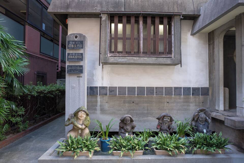 A building with a plaque, a window with bars, and statues with plants in front.