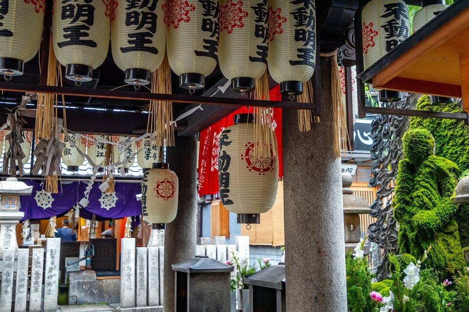 Traditional Japanese lanterns hanging indoors, surrounded by stone markers and greenery.