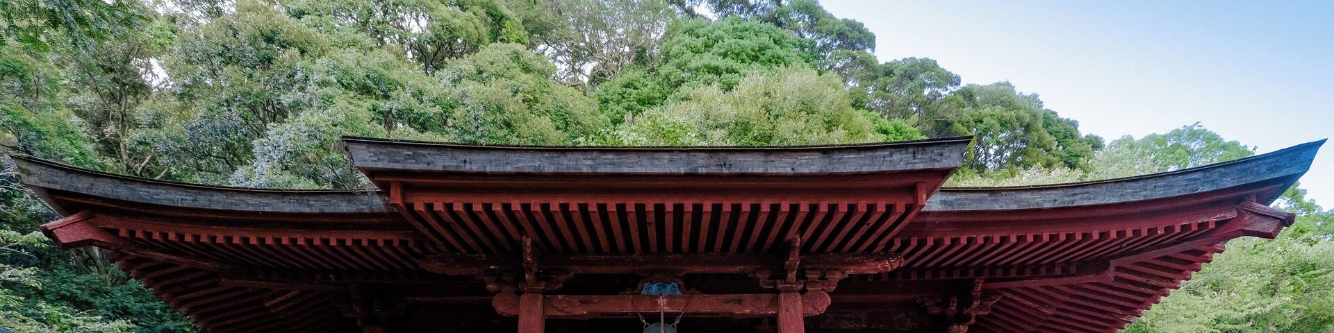 A traditional Japanese temple with red wooden architecture, a stone pathway, and a sign with Japanese characters.