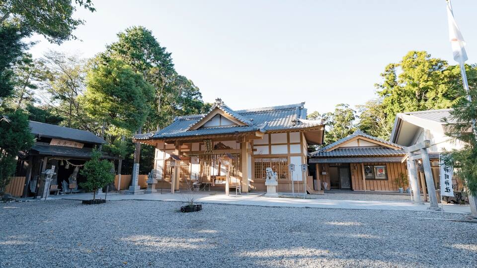 A traditional Japanese temple with a gravel courtyard, wooden buildings, and a flagpole.