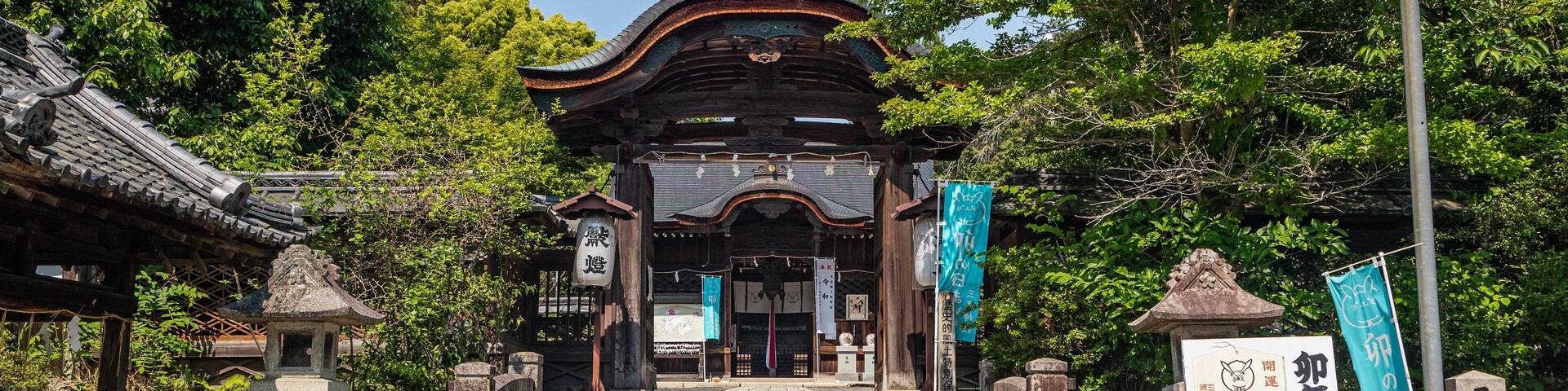 Entrada tradicional de un templo japonés, con un portón de madera, escalones de piedra e insignias.