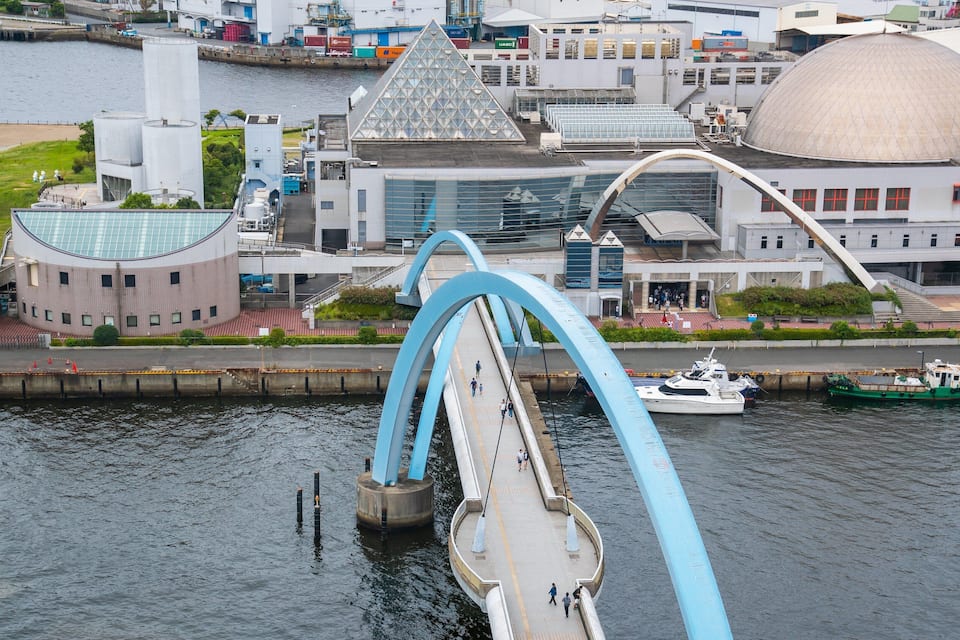 A bridge with blue arches over a river, a large building with a dome, and a green boat docked nearby.
