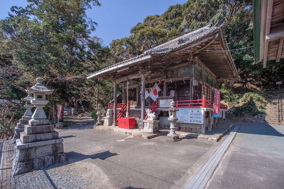 A traditional Japanese shrine with a tiled roof, stone lanterns, and a red railing.