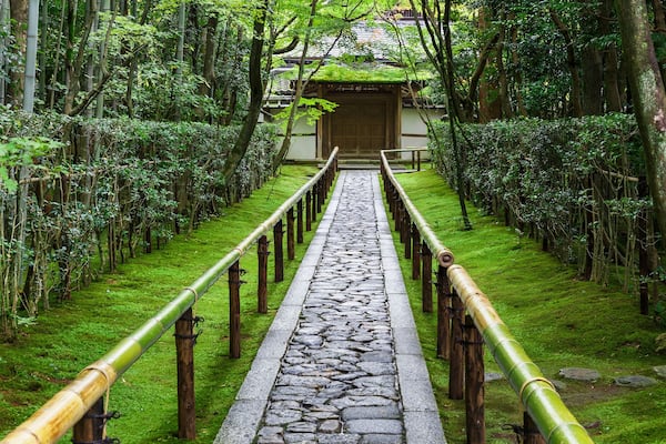 A stone pathway flanked by bamboo railings leading to a traditional wooden gate.