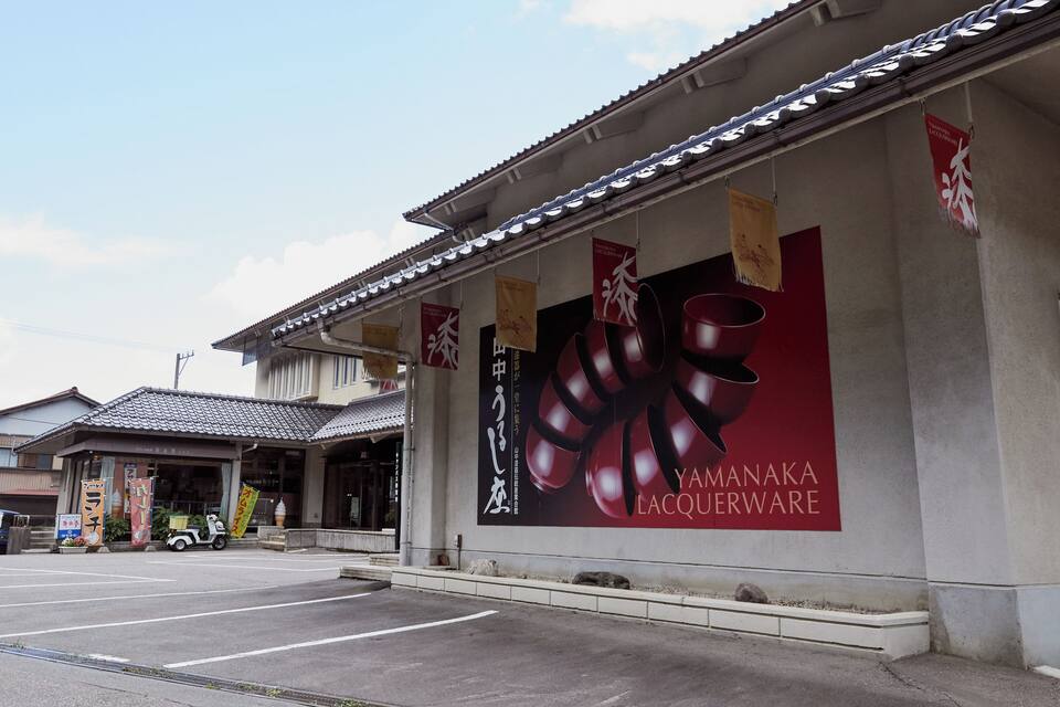 A building with a tiled roof and a large advertisement for Yamanaka Lacquerware. There are banners hanging from the roof and a small vehicle parked in front.
