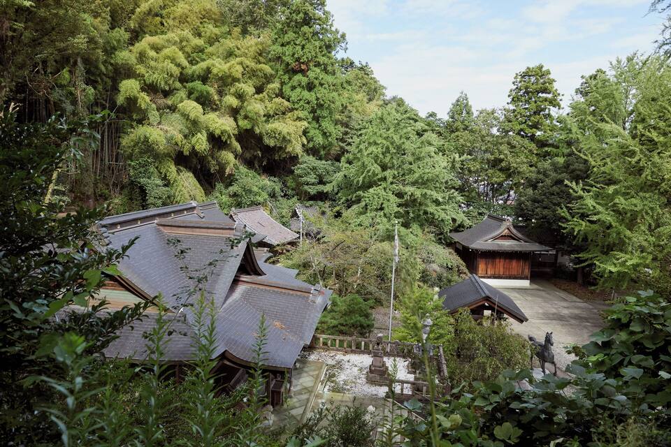 A traditional Japanese village with wooden houses, a stone lantern, and lush greenery.