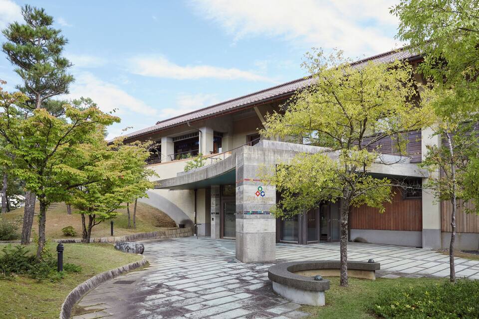 A modern building with a tiled entrance, surrounded by trees and a landscaped area.