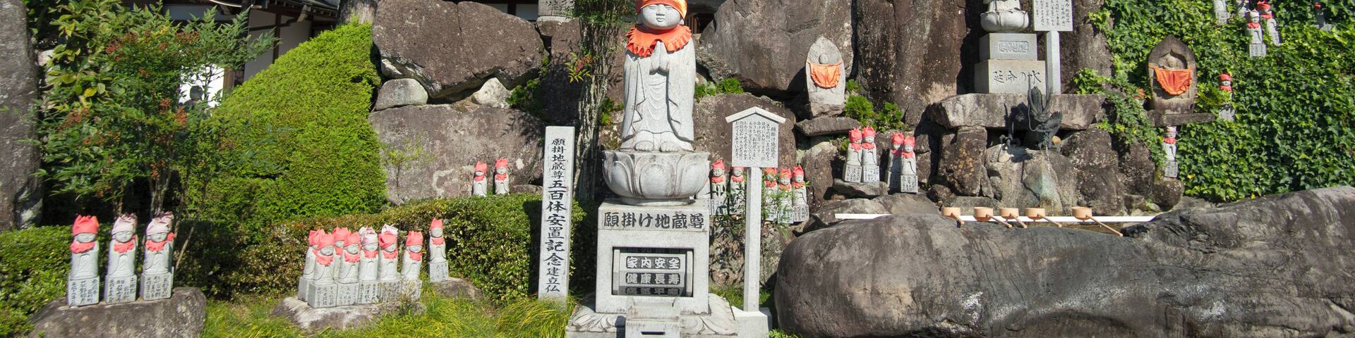A traditional Japanese temple with a red roof, stone statues, and a bell tower.