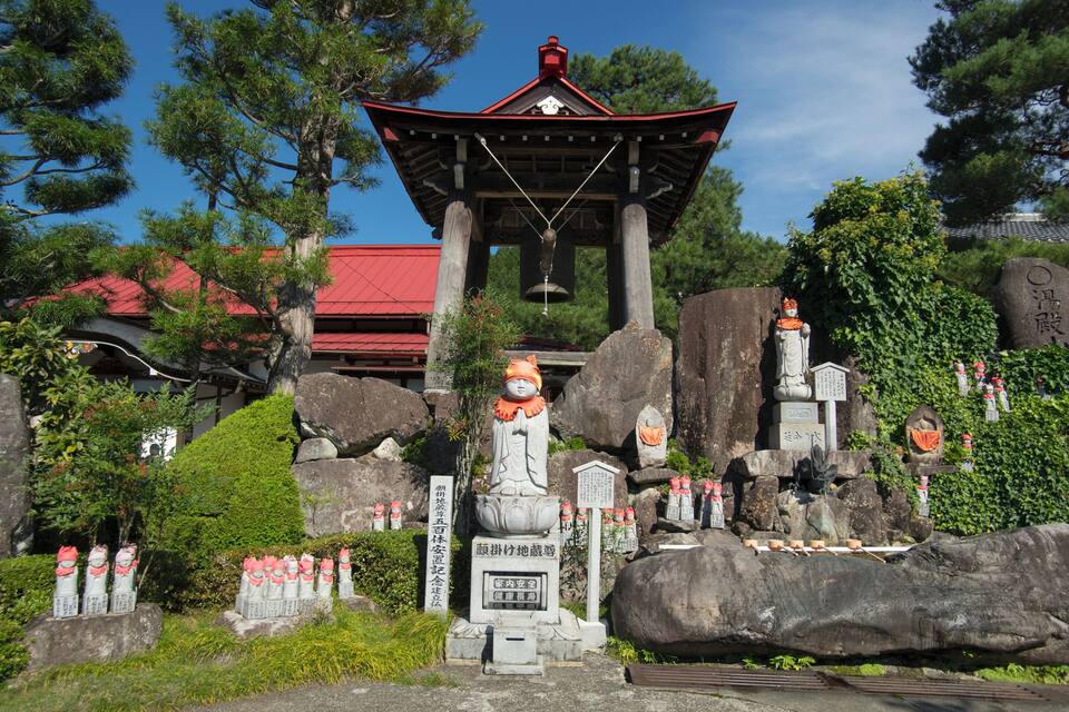 A traditional Japanese temple with a red roof, stone statues, and a bell tower.