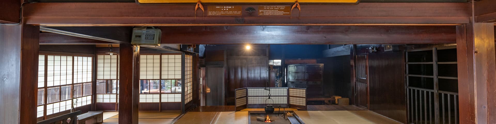 Una habitación tradicional japonesa con suelo de tatami, puertas correderas y un letrero colgante con caracteres japoneses.