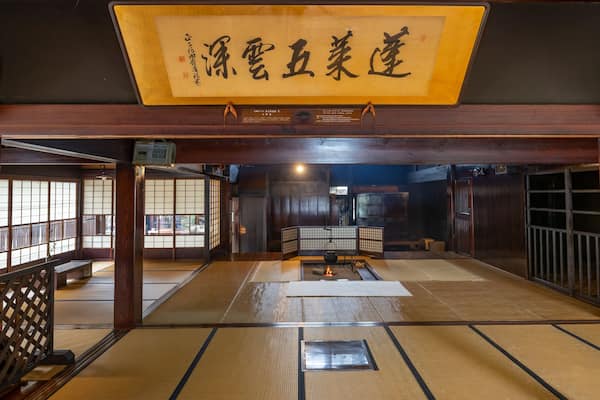Ein traditioneller japanischer Raum mit Tatami-Bodenbelag, Schiebetüren und einem hängenden Schild mit japanischen Schriftzeichen.