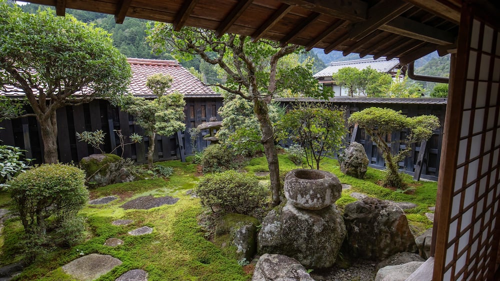 Un jardin japonais traditionnel, avec des rochers recouverts de mousse, des arbustes soigneusement taillés et une structure en bois.