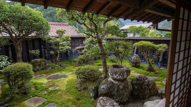 Un jardín japonés tradicional con rocas cubiertas de musgo, arbustos cuidadosamente recortados y una estructura de madera.