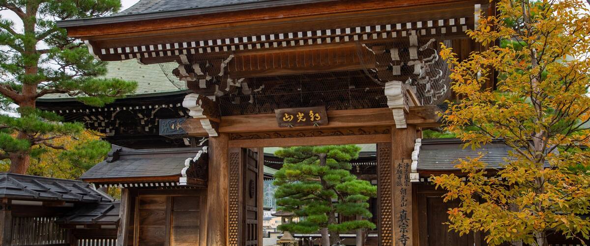 Une porte japonaise traditionnelle, ornée de sculptures complexes en bois et surmontée d’une enseigne.