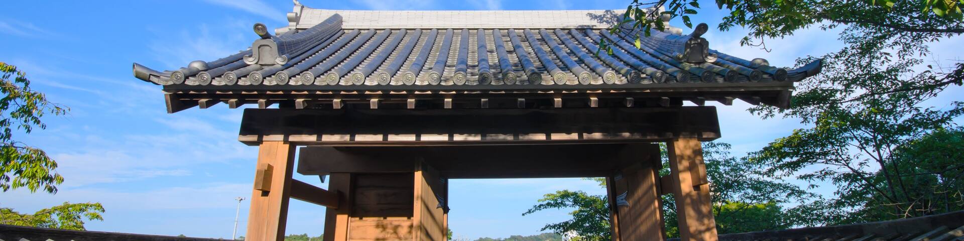 Un portón japonés tradicional con tejado de tejas, rodeado de paredes blancas y un sendero que lo atraviesa.