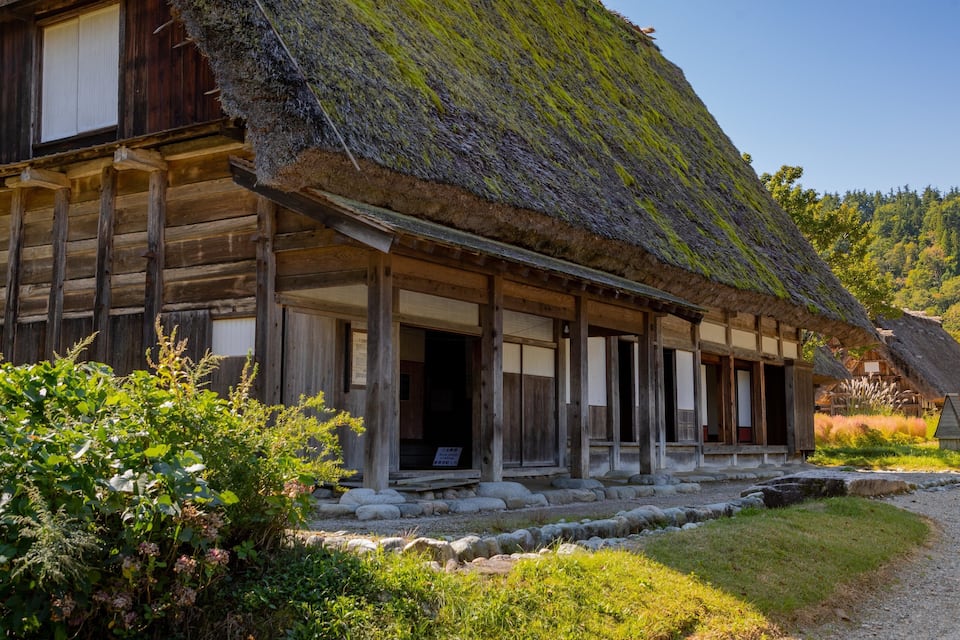 A traditional wooden house with a thatched roof and a stone pathway leading to it.