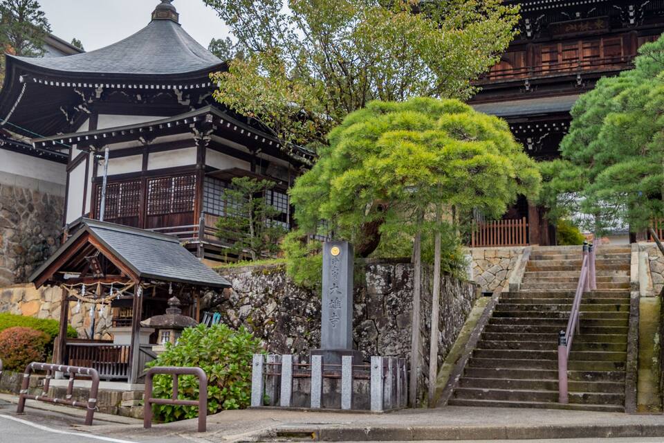 A traditional Japanese building with a curved roof, stone walls, and a stone staircase leading up to a wooden gate.