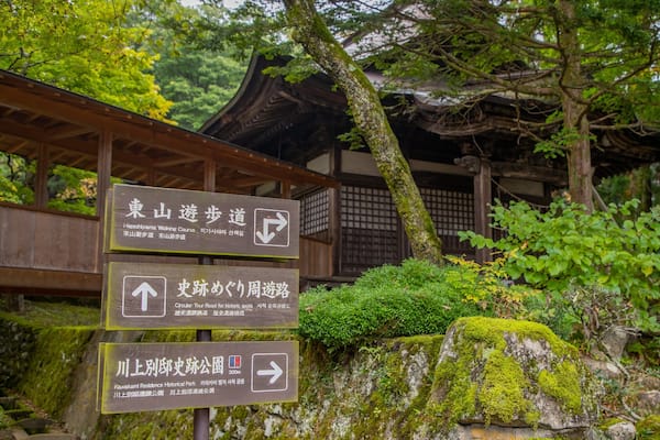 A traditional Japanese building surrounded by lush greenery and moss-covered rocks.