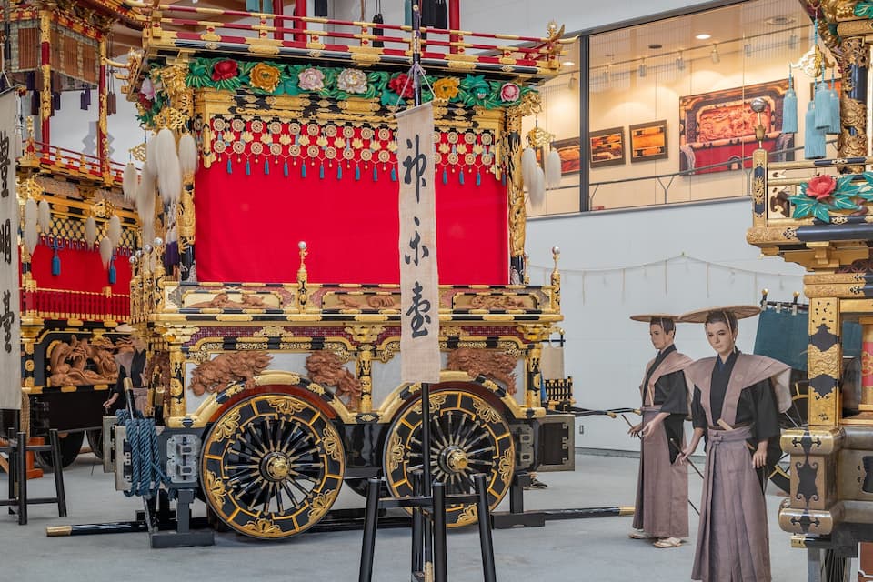 Uma carruagem chinesa tradicional com decorações elaboradas e duas pessoas vestidas com roupas da época.