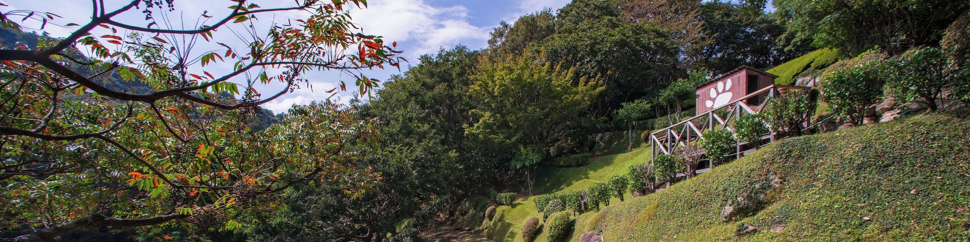 A landscaped garden with neatly trimmed hedges, a winding path, and a small building with a distinctive roof design.