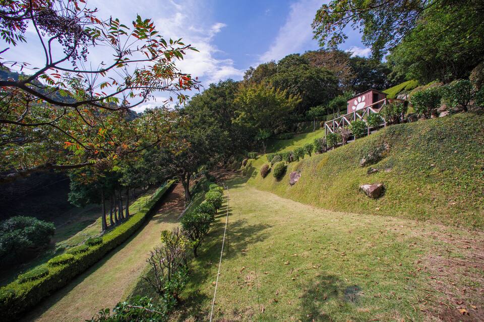A landscaped garden with neatly trimmed hedges, a winding path, and a small building with a distinctive roof design.
