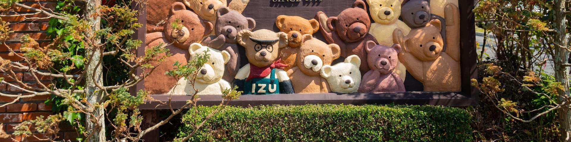 A sign for the Izu Teddy Bear Museum with various teddy bears displayed.