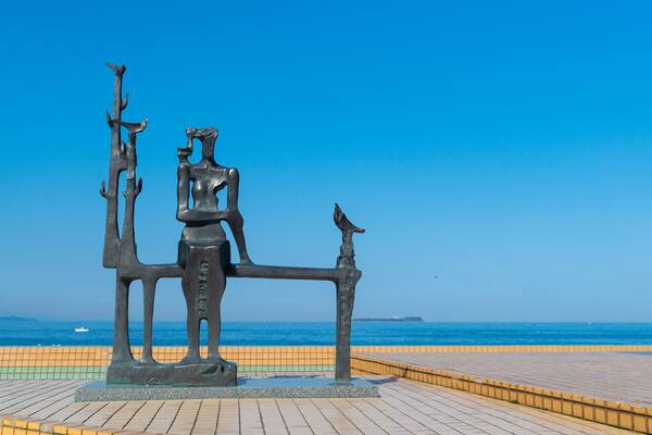 Escultura em bronze de uma mulher e um homem com um pássaro sentados num banco à beira-mar.