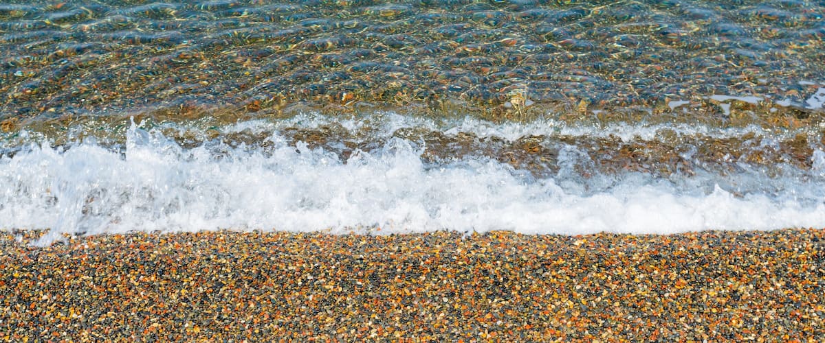 A pebbly beach with clear water and gentle waves.