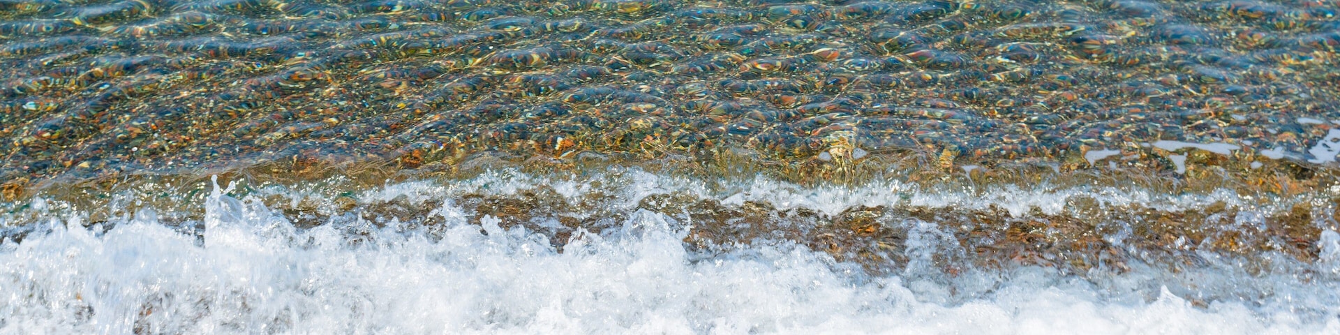 A pebbly beach with clear water and gentle waves.