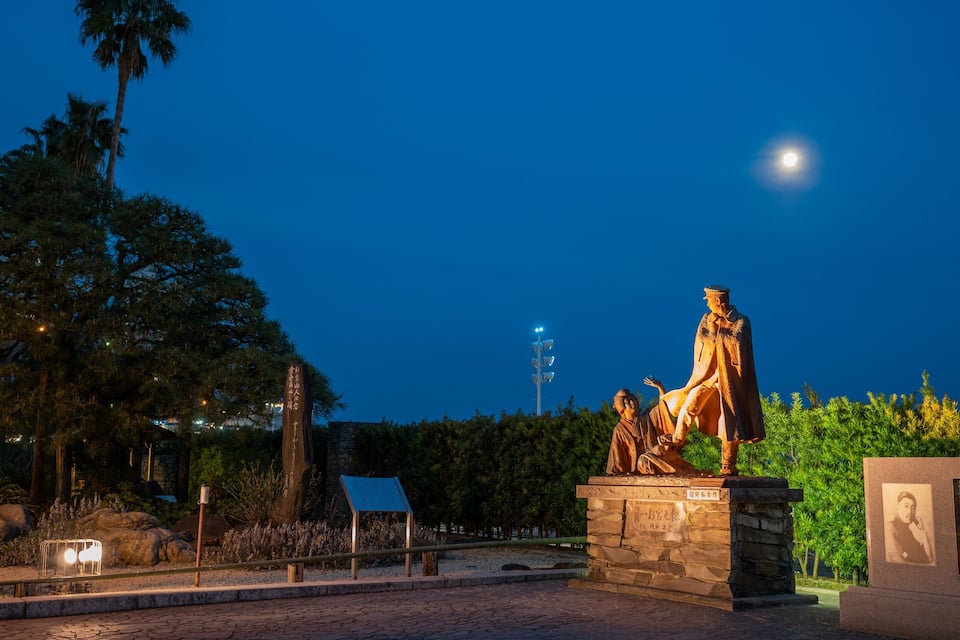 A statue of a man in traditional attire, a moon in the sky, and a sign with text.