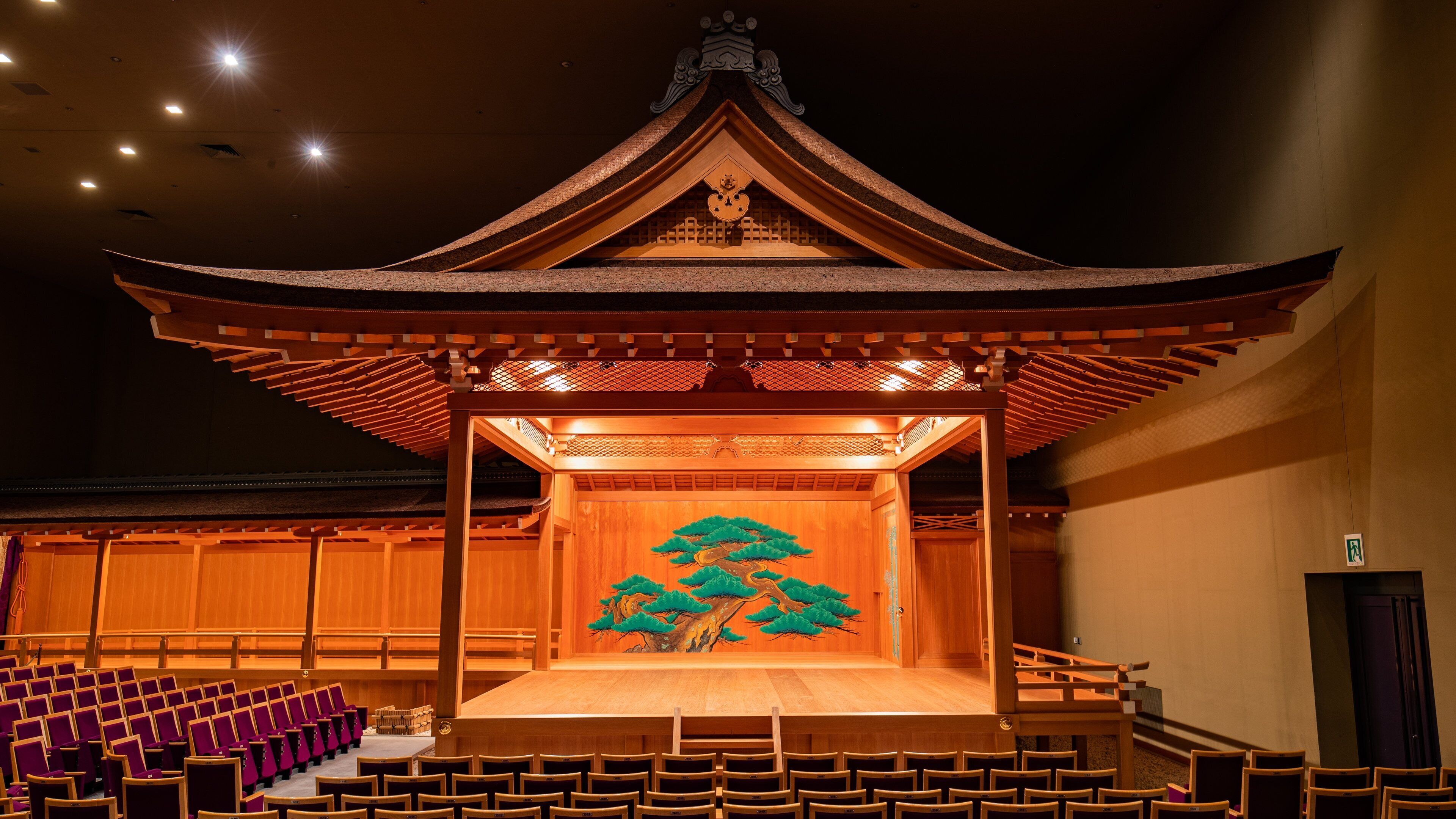 A traditional wooden stage with a painted tree mural, surrounded by rows of purple chairs.